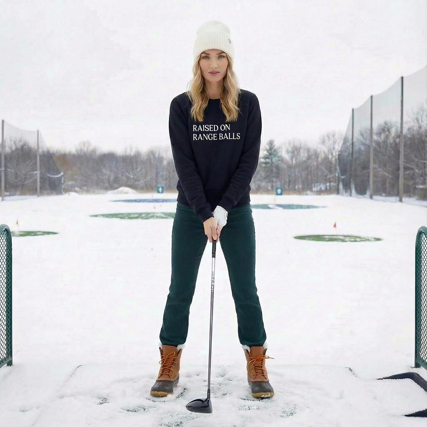 model at driving range wearing navy emyvale golf sweatshirt raised on range balls graphic
