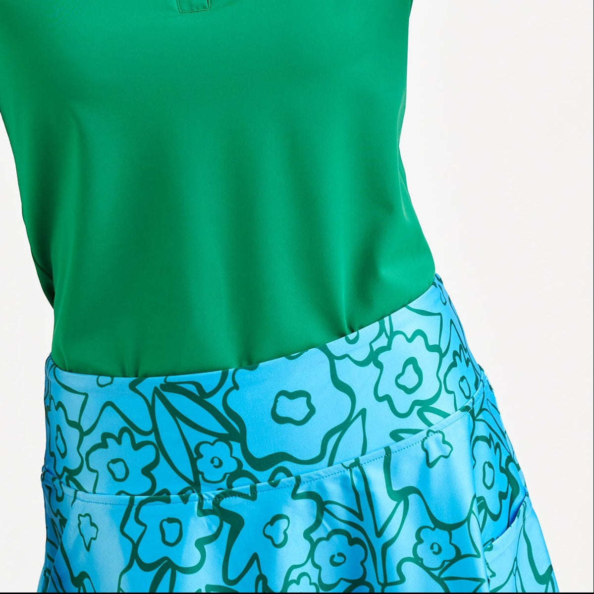 Woman wearing a green polo shirt and blue floral skirt on a white background