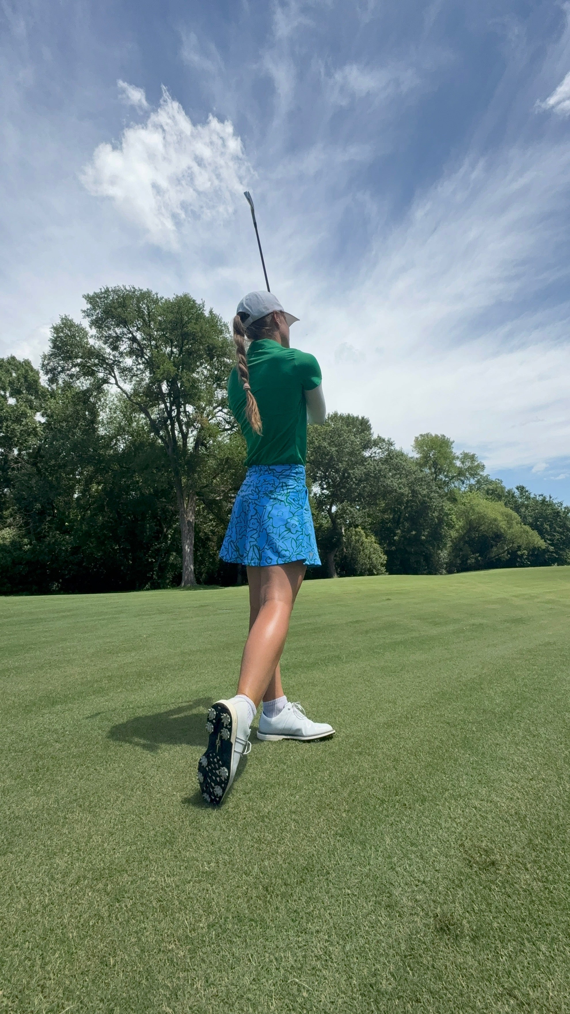 Woman wearing Emyvale Golf clothes playing golf on a green course with trees and blue sky in the background