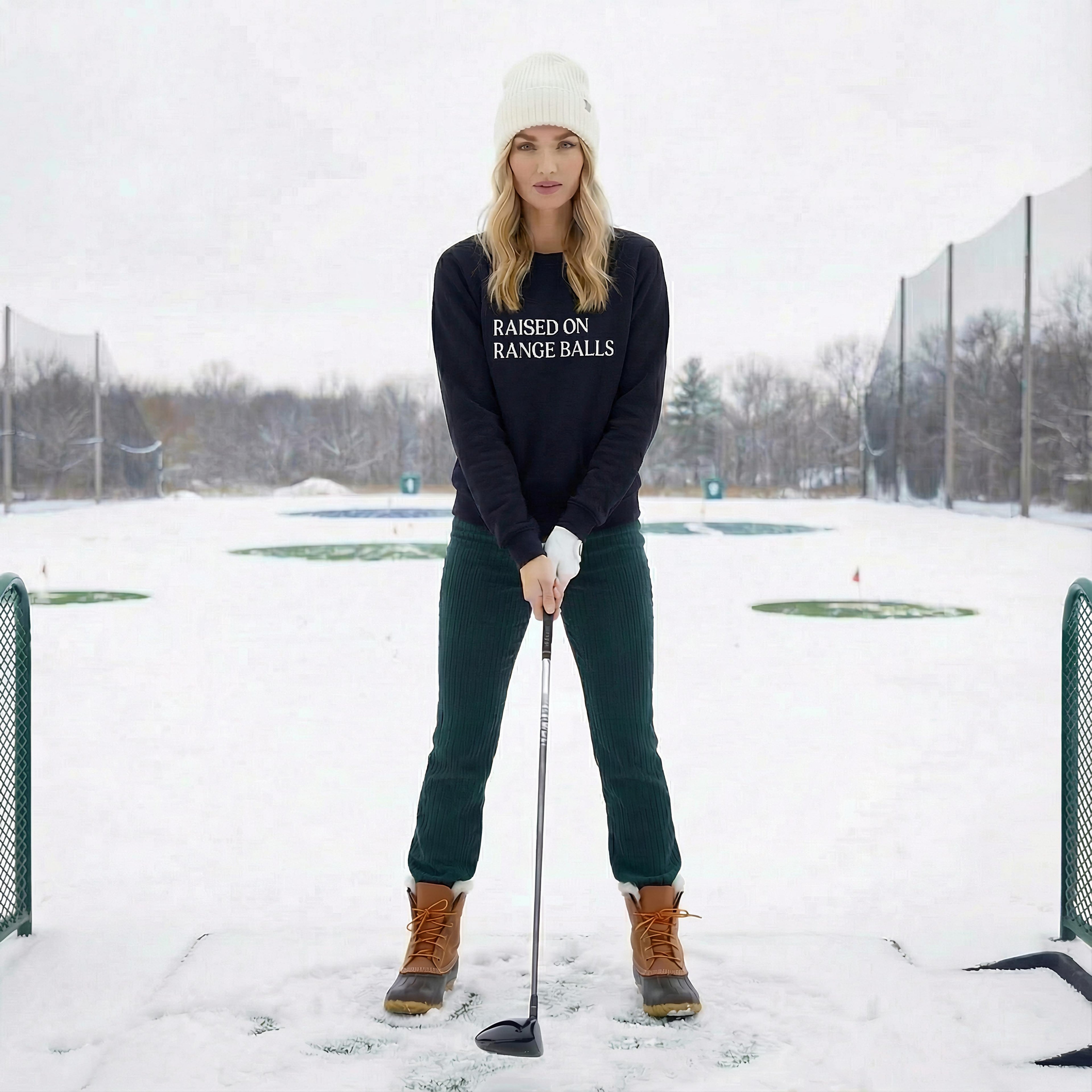 model at driving range wearing navy emyvale golf sweatshirt raised on range balls graphic